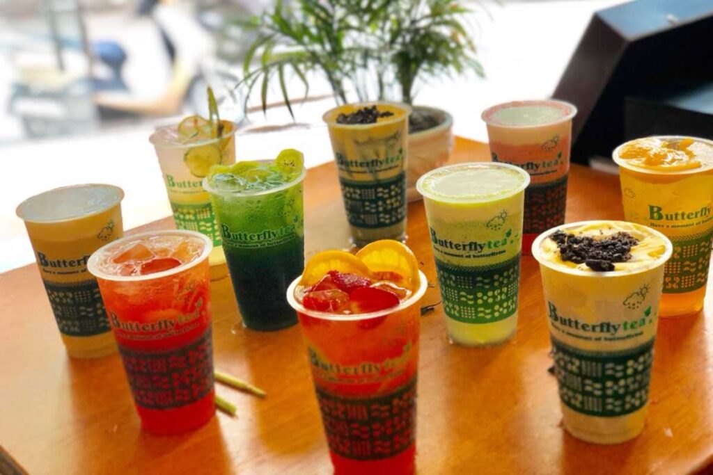 Hàng chục ly trà sữa sắc màu với thương hiệu Butterfly Tea được xếp trên bàn gỗ.